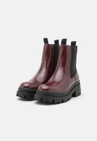 Bottines en cuir verni bordeaux avec des panneaux latéraux en élastique, semelles en caoutchouc noir épaisses et tirants pour un enfilage facile.