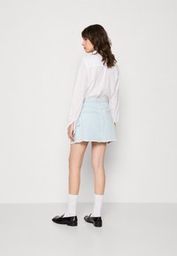 Hele sinise denim seelik frayed servaga ja kahe taga taskuga, koos valge pika varrukaga särgiga ja mustade loaferitega valgete sokkidega.