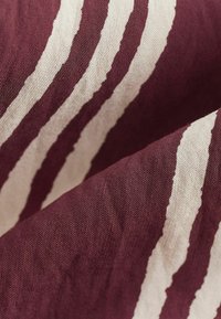 Tissu rayé bourgogne et crème, tissage texturé, présentant des lignes audacieuses et irrégulières avec une apparence légère et douce.