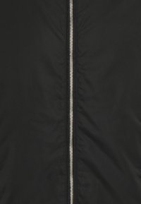 Černá zateplená bunda se stříbrným zipem uprostřed. Vyrobena z hladkého syntetického materiálu s nízkou hmotností.