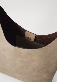 Beige fusk-suede toteväska med öppet topp, brun innerväska och tryckknappsstängning. Har en mjuk textur och minimalistisk design.