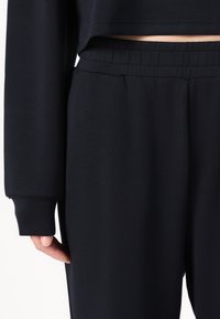Sötétkék pamut keverék sportos szett cropped topból és laza szabású nadrágból áll, melyek rugalmas derékkal és bordás mandzsettákkal rendelkeznek.