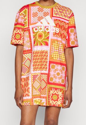 Kvinde iført kortærmet Adidas T-shirt-kjole med farverige geometriske og blomsteragtige blokmønstre i røde, pink, orange og gule nuancer.