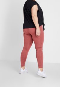 Mustapaita, jossa on lyhyet hihat ja solmunsauma vyötäröllä, yhdistetty punaisiin legginsseihin. Valkoiset urheilukengät viimeistelevät asun. Suoria pintoja.