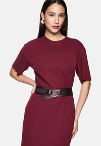 Bordeaux Kleid mit kurzen Ärmeln und einem lockeren Schnitt, tailliert mit einem breiten schwarzen Gürtel mit einer strukturierten goldenen Schnalle.