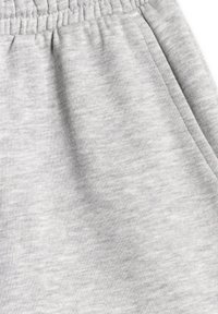 Tissu gris clair en gros plan montrant la ceinture élastique et les détails des poches latérales sur un pantalon ou un short décontracté.