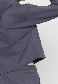 Dark gray cropped hoodie made of soft, lightweight fabric. Features a relaxed fit, long sleeves, and a smooth texture.