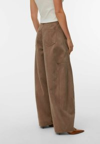 Pantalon large en velours côtelé marron avec nervures verticales, deux poches arrière et coupe décontractée, associé à des talons pointus marron.