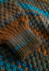 Mehrfarbiger Strickstoff mit blauen, braunen und orangen Garnen in einem gerippten und gemusterten Textur.