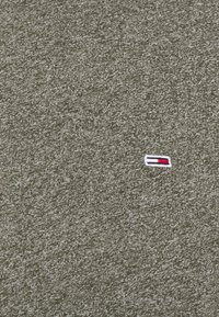 Olivově zelený svetr s texturovaným pleteným vzorem obsahuje malé vyšívané logo v červené, bílé a modré barvě. Jednoduchý design a měkká tkanina.