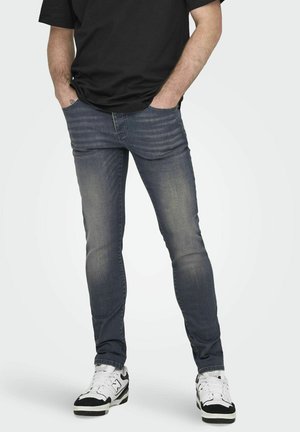 Vaqueros skinny de color azul oscuro con una textura suave, desvanecidos en las piernas, bolsillos frontales y un diseño de tiro medio. Combinados con zapatillas blancas y negras.