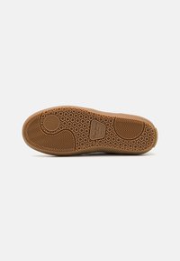 Suela de zapato de goma en marrón claro con un patrón de panal, que presenta detalles de textura circular y de espiga para un mejor agarre y tracción.