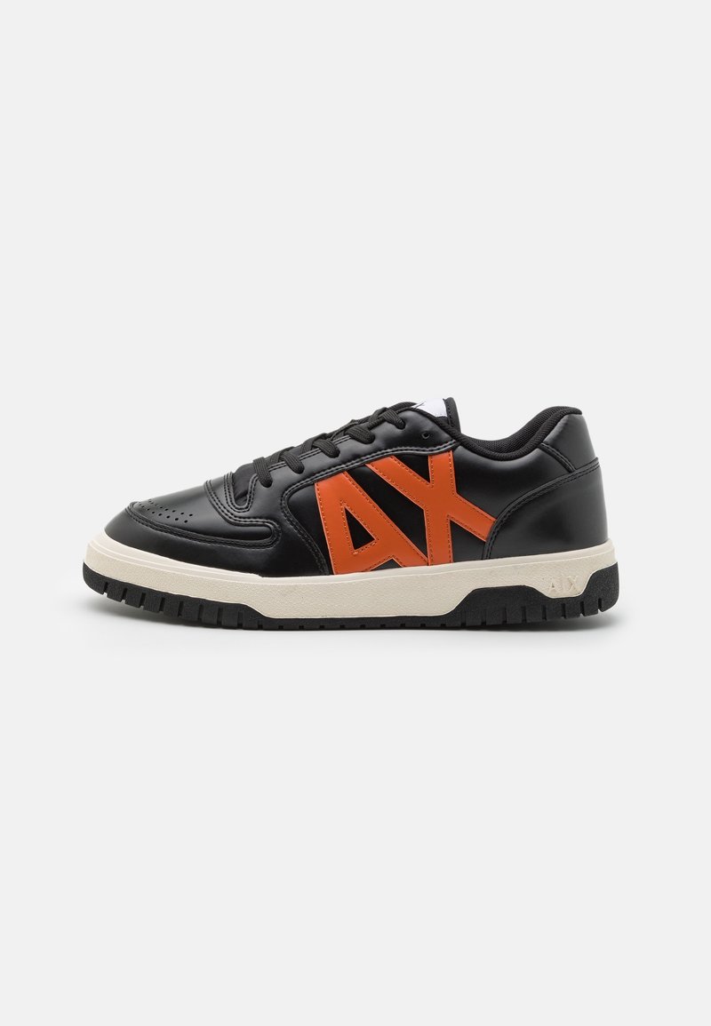 Svart lågtopp sneakers med vit sula och stor orange "AX"-logotyp på sidan, med snörning och texturerad sula.
