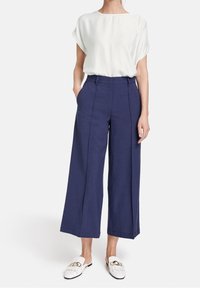 Witte blouse met korte mouwen, gecombineerd met marineblauwe wijde broek. Witte instappers hebben een decoratieve hardwareaccent.