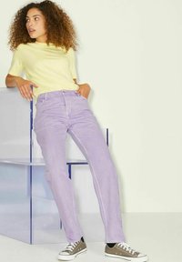 Top amarelo claro de manga curta combinado com jeans lavanda de cintura alta. Os jeans têm um design de perna reta e cinco bolsos. Ténis castanhos completam o visual.