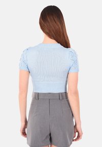Top lavorato a maglia azzurro chiaro a maniche corte con un design aderente. Presenta un orlo a coste e dettagli intricati sulle spalle. Abbinato a pantaloni corti grigi.