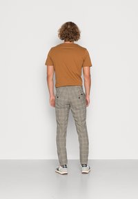 Braunes kurzärmeliges Hemd kombiniert mit karierten grauen Hosen. Die Hose hat eine schmale Passform und zwei Gesäßtaschen. Legere Sneaker runden den Look ab.