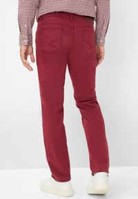 Pantaloni in cotone rossi con vestibilità slim, dotati di due tasche posteriori e una texture liscia. Abbinati a sneaker bianche per un contrasto.