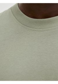 Jasnozielona bawełniana koszulka z ribowanym okrągłym dekoltem i gładką teksturą, zbliżenie na szczegóły materiału.