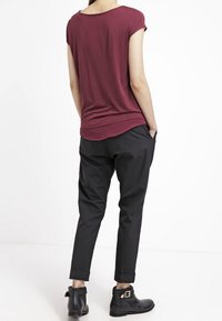 Haut bordeaux à manches courtes associé à un pantalon noir fuselé. Le pantalon présente des revers et est porté avec des bottines noires à hauteur de cheville ornées de boucles métalliques.