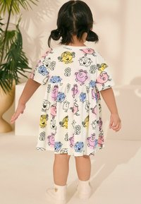 Vitt bomullsklänning med en lekfull flerfärgad tecknad design som visar karaktärer och blommor. Lös passform, korta ärmar och volangkjol.