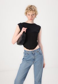 Crop top noir avec un design structuré et des manches courtes, associé à un jean taille haute bleu clair. Portant un sac à bandoulière noir arrondi et clouté.