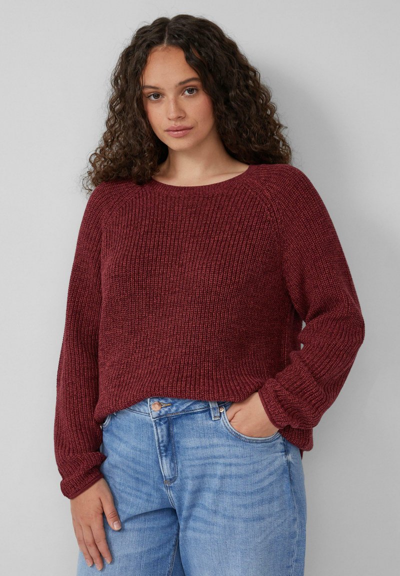 Burgunderfarbener Strickpullover mit Rundhalsausschnitt, gerippter Textur und langen Ärmeln, kombiniert mit hellblauen Jeans.