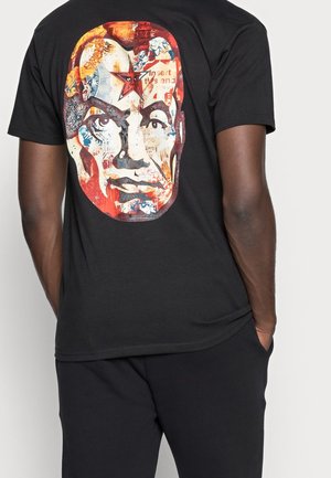 Schwarzes T-Shirt mit einem grafischen Druck auf der Rückseite, der ein Gesicht zeigt, das mit lebendigen Farben und Texturen gestaltet ist, einschließlich roter und blauer Akzente.