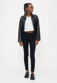 Fekete műbőr dzseki, fehér, fodros szélű cropped top, fekete, magas derekú skinny farmernadrág gombos részletekkel, fekete loaferek.