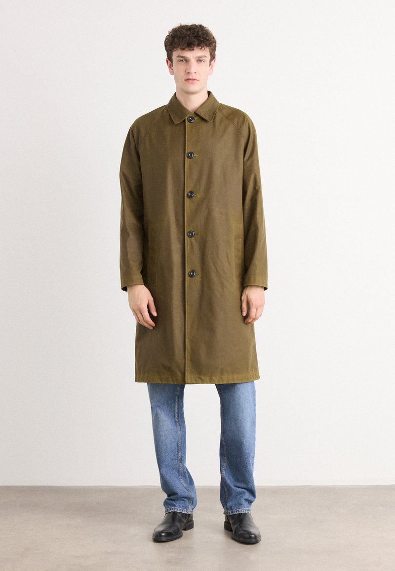 Olive green long coat with a button-down front, featuring a shirt collar and two side pockets, paired with light blue jeans and black shoes.