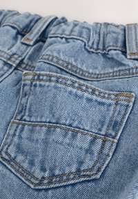 Primer plano de vaqueros de mezclilla azul claro con bolsillo trasero visible y detalles de costuras en la cintura elástica.
