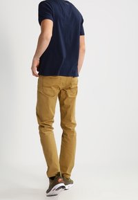 Beiga chinos med smal passform, två bakfickor och subtila sömnadsdetaljer; kombinerade med en marinblå t-shirt och grå träningsskor.