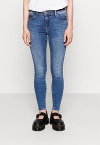 Skinny jeans in medium blue denim with a faded design. Features a five-pocket style, belt loops, and a button closure. Worn with black shoes.