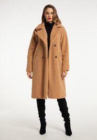 Brown, fluffy fabric coat with a double-breasted design, large collar, side pockets, and black buttons, worn over a black turtleneck.