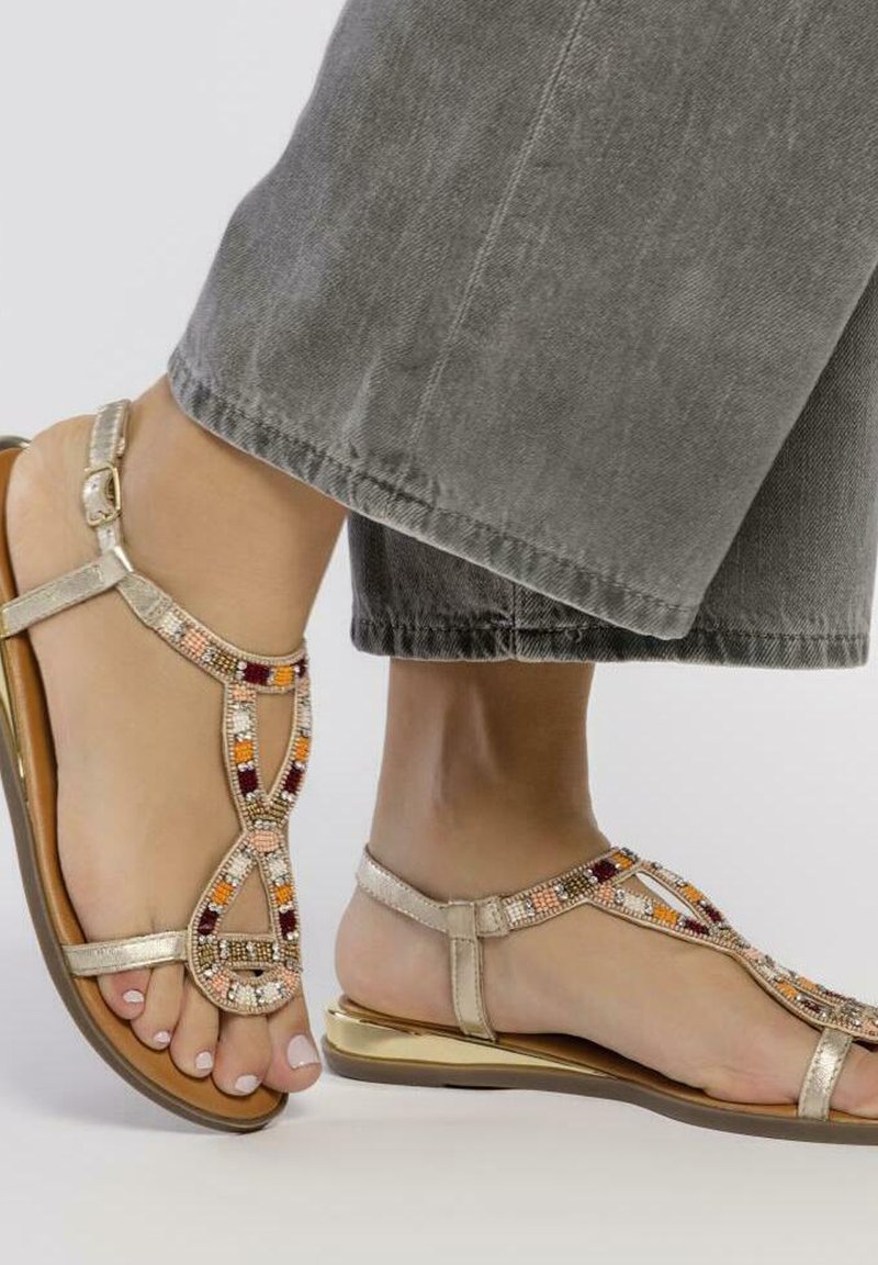 Sandales couleur or avec des accents de perles en orange, rouge et crème. Design plat, boucle pour les orteils, bride de cheville et semelle texturée.