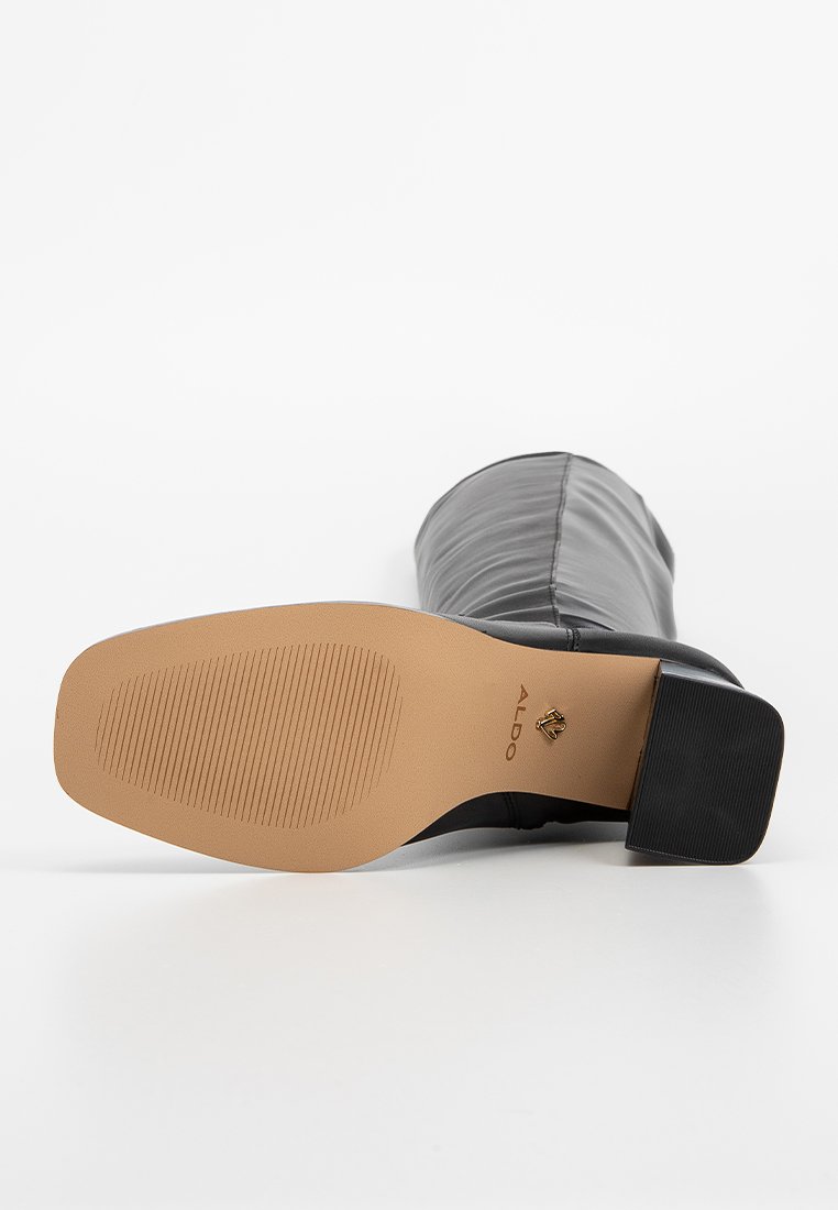 Stivale alla caviglia in pelle nera con punta arrotondata, tomaia testurizzata e suola in gomma marrone chiaro con scanalature orizzontali e tacco basso.