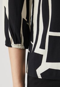 Top astratto in bianco e nero con maniche a tre quarti, caratterizzato da polsini elasticizzati e una texture di tessuto leggera e morbida.