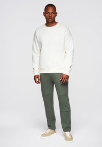 Kremowy sweter z okrągłym dekoltem, w połączeniu z oliwkowo-zielonymi joggerami z przeszyciami. Sneakersy w beżowo-białej kolorystyce.