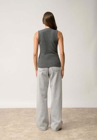 Top sin mangas gris hecho de un material suave, combinado con unos jeans de pierna ancha en gris claro. El conjunto presenta una silueta ajustada y líneas limpias.