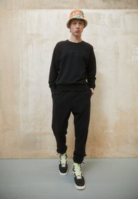 Must värvi särk ja dressipüksid, mis on valmistatud pehmest kangast, koos mustade kõrge säärega spordijalatsitega, millel on rohelised paelad, ning värvilise ämberkübara. 