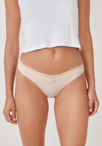 Culotte hipster beige avec une texture côtelée, une dentelle en bordure et un petit nœud au centre à l'avant. Conçue pour un ajustement confortable.