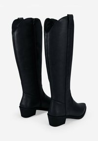 Botas de cuero negro hasta la rodilla con punta puntiaguda, cremallera lateral y un tacón bajo. Textura suave con un detalle de costura mínimo.