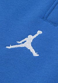 Blauwe gebreide stof met een witte geborduurde silhouet van een springende figuur, die doet denken aan een basketballer in beweging.