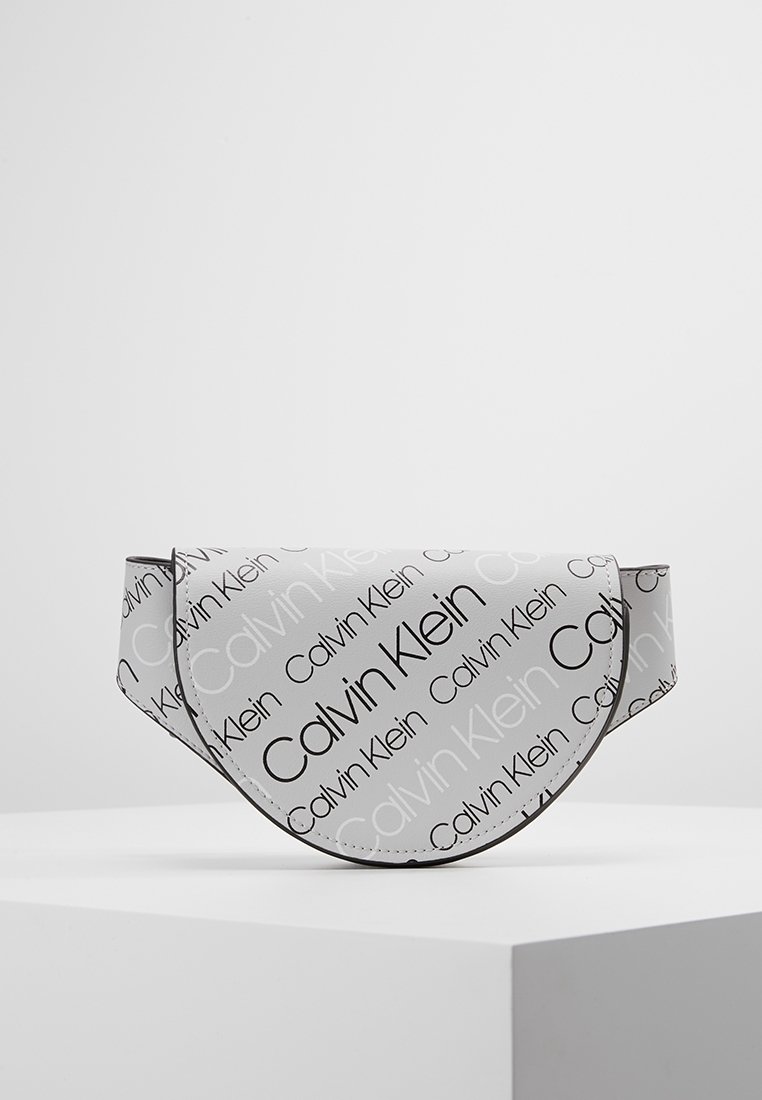 Calvin Klein-väska i vitt syntetmaterial, med en rundad klaffdesign. Svart logotext tryckt över ytan, med kontrasterande sömmar.