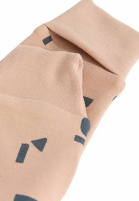 Strumpor i mjuk rosa tyg, med ribbad struktur och mörkblå geometriska mönster, inklusive trianglar och cirklar.
