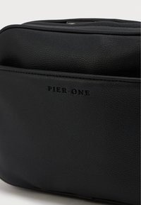 Melnas ādas soma ar strukturētu virsmu, diskreto zīmolu un elegantu dizainu ar plūstošu formu un minimāliem piederumiem.