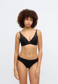 Μαύρο σουτιέν από δαντέλα με σχήμα κώνου και floral σχέδιο, διαθέτοντας ρυθμιζόμενες τιράντες. Συνδυάζεται με αντίστοιχες μαύρες σλιπ με δαντελένιες λεπτομέρειες.