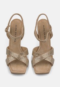 Beżowe zamszowe sandały z kwadratowym noskiem oraz krzyżującymi się paskami, ozdobione małymi metalicznymi ćwiekami; regulowany pasek na kostkę z okrągłą klamrą.