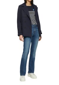 Marineblaues, doppelt knöpfen Jacket über einem gestreiften navy- und weißen Oberteil, kombiniert mit hellblauen Schlagjeans und weißen Plateausneakern.