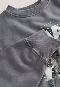 Dunkelgrauer Pullover mit geripptem Rundhalsausschnitt und Bündchen. Verfügt über ein strukturiertes Druckdesign mit weißen Akzenten. Der Stoff hat eine weiche Oberfläche.